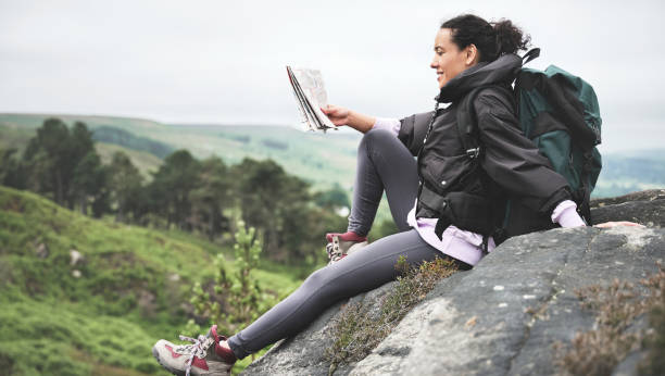 toma de cuerpo entero de una atractiva joven sentada sola en una roca y leyendo un mapa durante una caminata - map uk hiking reading fotografías e imágenes de stock