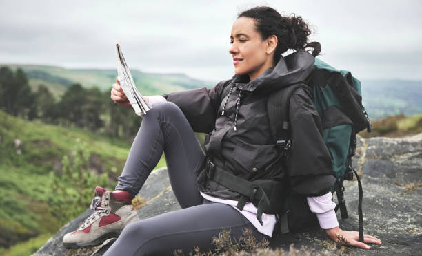 foto de una atractiva joven sentada en una roca y luciendo contemplativa mientras lee un mapa durante una caminata - map uk hiking reading fotografías e imágenes de stock