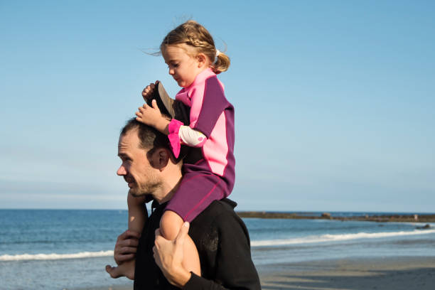 Father holding daughter on his shoulders on the beach. Dad is in his forties, and girl is 4 year’s old. Horizontal waist up outdoors shot with copy space.