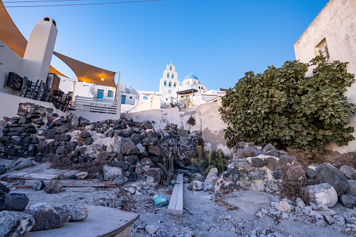 Church of St (Agia) Theodosia in Pyrgos Kallistis on Santorini, Greece, with volcanic rubble in the foreground and a restaurant.