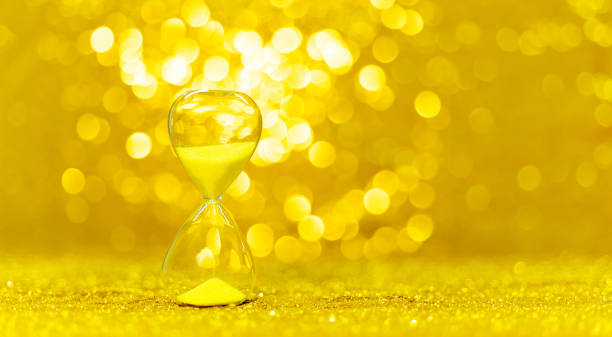 Modern hourglass on shiny golden background.