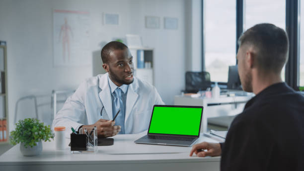 ein afroamerikanischer arzt erklärt einem patienten die diagnose auf einem computer mit green screen in einer gesundheitsklinik. assistent im weißen laborkittel liest die krankengeschichte im krankenhausbüro. - computer lab green office computer stock-fotos und bilder