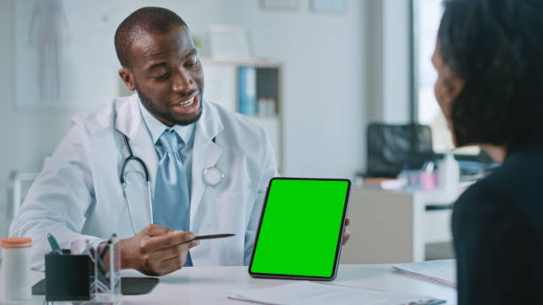 ein afroamerikanischer arzt erklärt einem patienten die diagnose auf einem tablet mit green screen in einer gesundheitsklinik. assistent im weißen laborkittel liest die krankengeschichte im krankenhausbüro. - computer lab green office computer stock-fotos und bilder