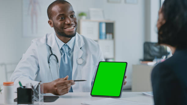ein afroamerikanischer arzt erklärt einem patienten die diagnose auf einem tablet mit green screen in einer gesundheitsklinik. assistent im weißen laborkittel liest die krankengeschichte im krankenhausbüro. - computer lab green office computer stock-fotos und bilder