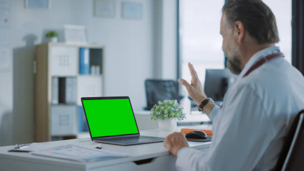 hausarzt macht einen videoanruf mit patient auf einem computer mit green screen display in einer gesundheitsklinik. assistent im laborkittel spricht über gesundheitsprobleme im krankenhausbüro. - computer lab green office computer stock-fotos und bilder