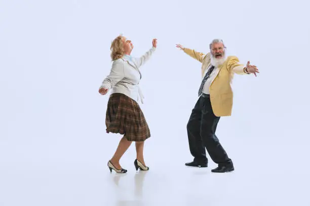 Photo of Two retro styled dancers, senior man and woman in vintage attire dancing rock-and-roll isolated on white background