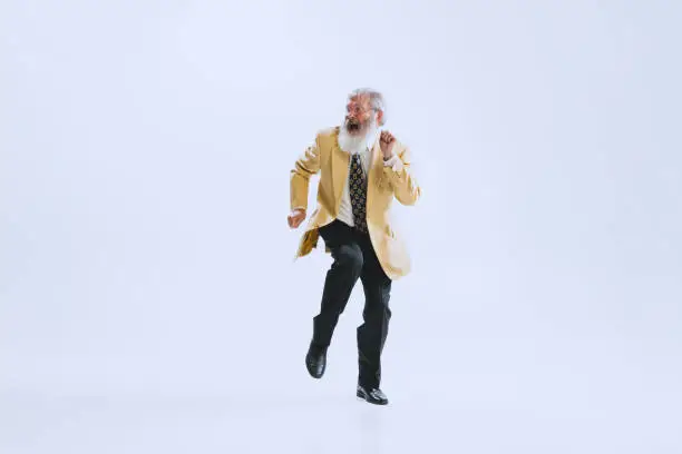 Photo of Portrait of emotional senior man in retro style clothes, vintage outfit dancing rock-and-roll isolated on white background