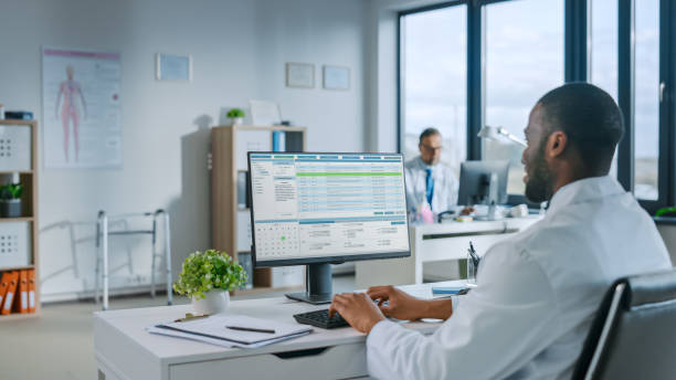 istock Experienced African American Male Doctor Wearing White Coat Working on Personal Computer at His Office. Medical Health Care Professional Working with Test Results, Patient Treatment Planning. 1355655792