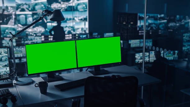 istock Two Digital Computer Screens with a Green Mock Up Chromakey in Modern Monitoring Office. Control Room with Specialists and Managers Sit in Front of Computers. 1355656559