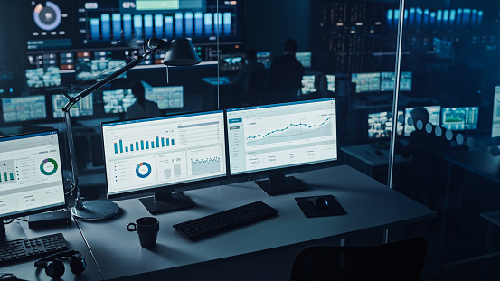 Two Digital Computer Screens with Financial Analytical Data in Modern Monitoring Office. Control Room with Finance Specialists Sit in Front of Computers.