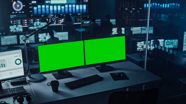 istock Two Digital Computer Screens with a Green Mock Up Chromakey in Modern Monitoring Office. Control Room with Specialists and Managers Sit in Front of Computers. 1355657080