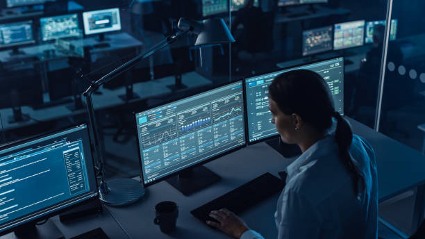 istock Female Software Engineer Working in a Modern Monitoring Office with Live Analysis Feed with Charts on a Big Digital Screen. Monitoring Room Big Data Scientists and Managers Sit in Front of Computers. 1355657084