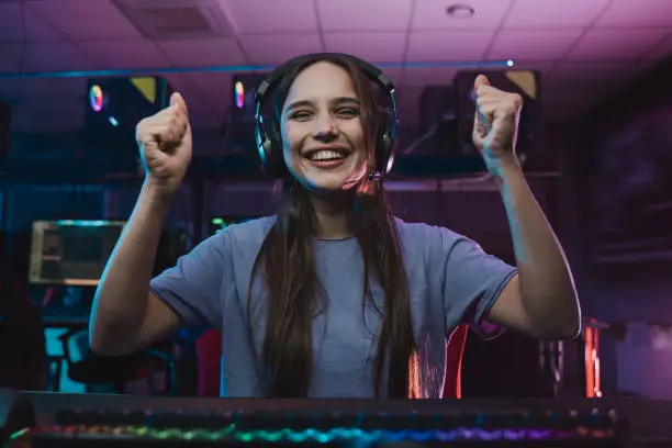 Close-up of the professional female video game player at e sports tournament. Cyber athlete wearing headphones rejoicing emotionally