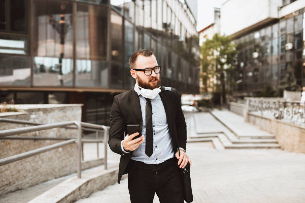 istock Smiling Businessman With Face Mask Using Smartphone To Find Conference Building 1355659262