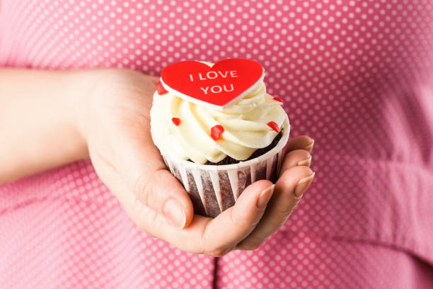 gâteau de cœur en forme dans les mains avec l’inscription i love you sur fond rose. cupcake en forme de gros plan - candy heart candy i love you heart shape photos et images de collection