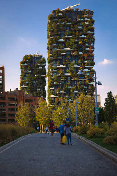 MILAN, ITALY - September 11, 2021: Bosco Verticale (Vertical Forest) is a pair of residential towers in the Porta Nuova district of Milan, Italy, between Via Gaetano de Castillia and Via Federico Confalonieri near Milano Porta Garibaldi railway station. They have a height of 111 metres (364 ft) and 76 metres (249 ft) and contain more than 900 trees (approximately 550 and 350 in the first and second towers, respectively) on 8,900 square metres (96,000 sq ft) of terraces. Within the complex is an 11-storey office building; its facade does not include plants.