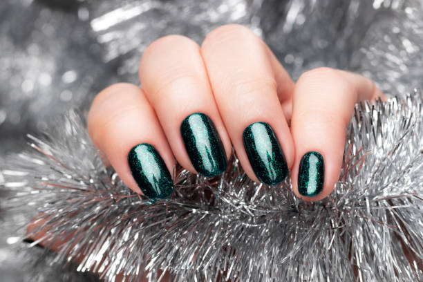 istock Hand with green glittered nails with silver tinsel 1355665476