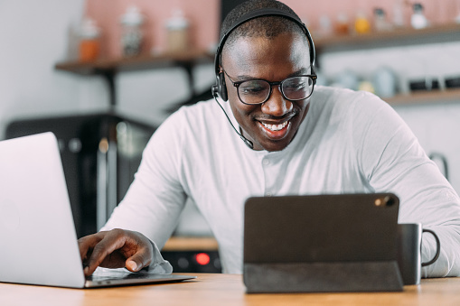 Shot of handsome young businessman working from home. Photo of a young african-american man using a laptop, digital tablet and headset while working at home.
