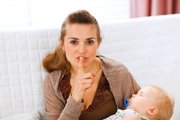 istock Young mama holding sleeping baby and showing shh gesture 135566554