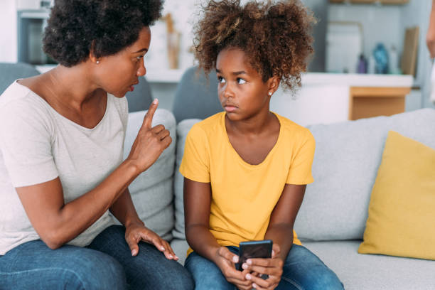 Mother arguing with daughter over use of mobile phone. Shot of a young girl looking upset while being scolded by her mother at home. scolding stock pictures, royalty-free photos & images