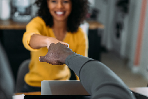 Shot of smiling young african-american couple working at home on laptops and doing fist bump greeting.