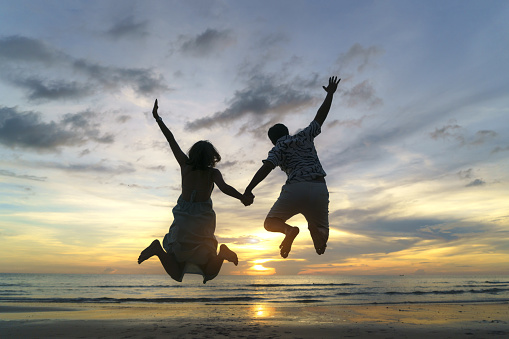 Asian couple jumping on the beach near sea with beautiful sunset, Couple on vacation in summer holidays concept