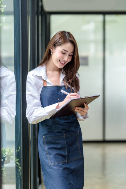 Beautiful young Asian woman entrepreneur standing taking note beside a large mirror.