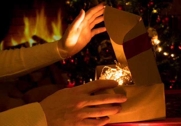istock Woman's hands opening christmas gift box on a fireplace and christmas lights background 1355670017
