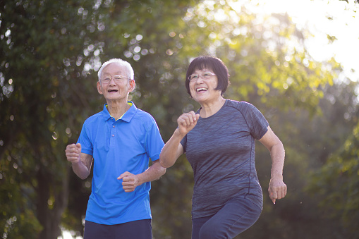 Asian Chinese active senior man and wife jogging side by side at morning in public park