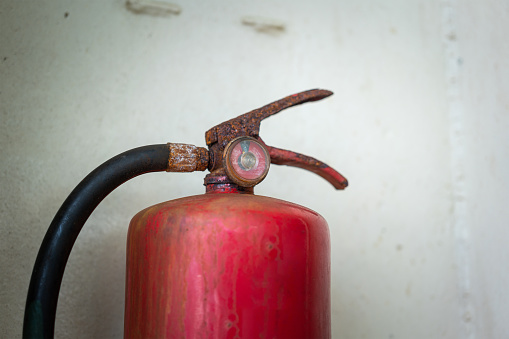 A very old chemical fire extinguisher which rusty handle and dirty pressure gauge. Emergency equipment object photo. Selective focus at pressure gauge.