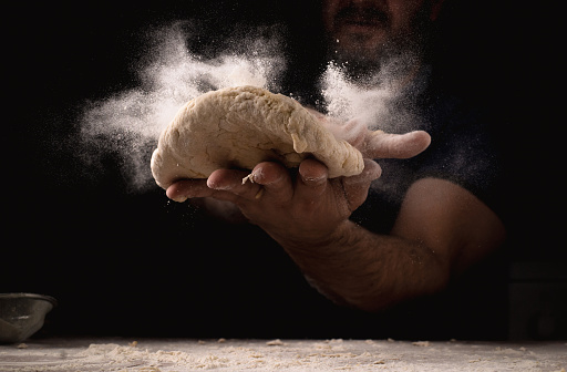 Explosion of flour in male hands and dough on a dark background. Dough preparation, cooking concept.