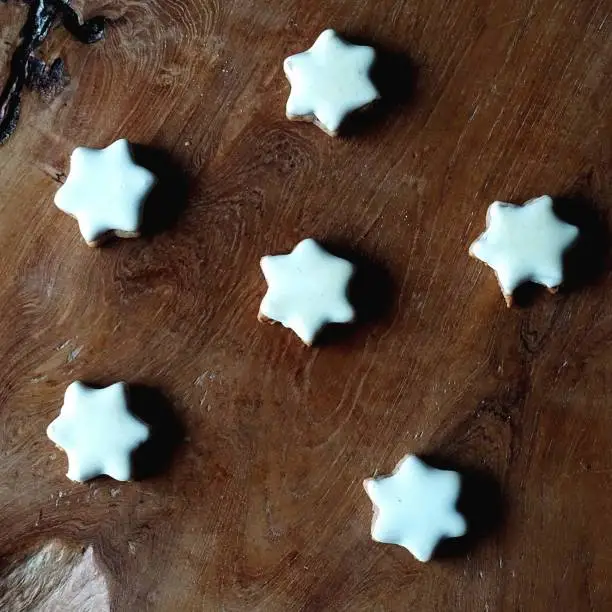 Cinnamon stars baked at Christmas time lie appetizing arranged on a board made of solid wood.  The colors of the cool white sugar layer and the warm brown holtisch form a nice contrast. The big picture is an invitation to snack. Photography has an unusual format.
