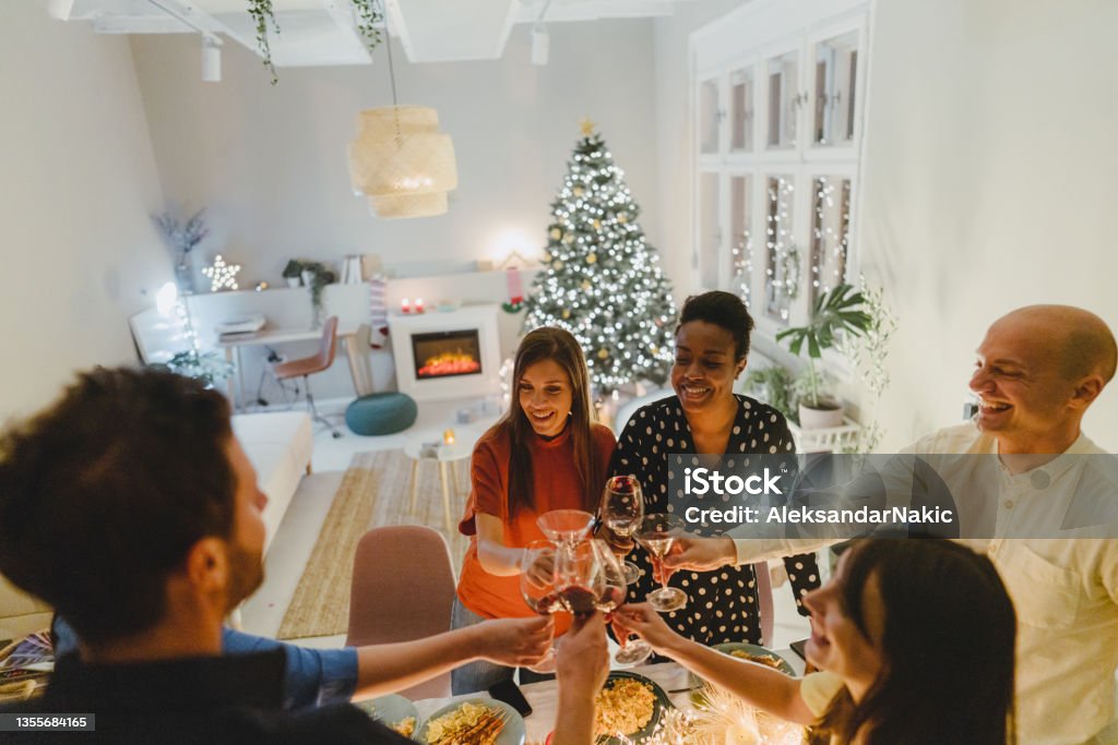 Merry Christmas everybody! Photo of a couple of multiracial group of friends, having Christmas dinner party together at home, toasting  to their friendship Christmas Stock Photo