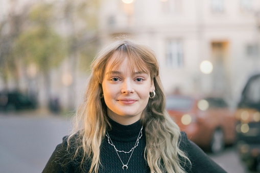 Portrait of a beautiful young woman standing outdoors. Caucasian female with blond hair standing on city street and looking at camera.