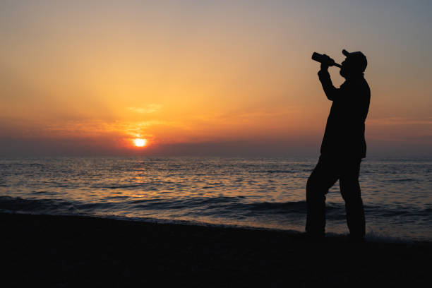 istock a man in a cap drinks wine from a bottle during a sunset at the sea 1355685018