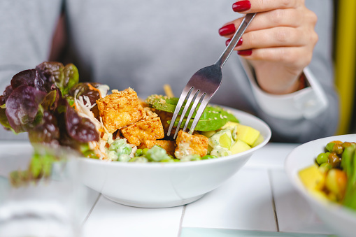 Woman eating a vegan salad bowl with tofu, avocado and edamame at the restaurant