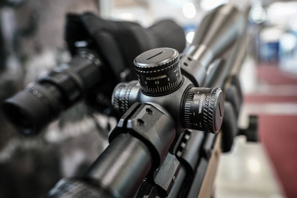 Black shooting scope optics mounted on rifle displayed at weapons exhibition fair, closeup detail to adjustment knobs.