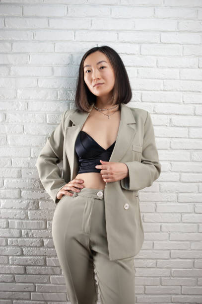 a fashionable asian woman in a stylish pantsuit poses against a white brick wall - fashion fashion model asian ethnicity tall imagens e fotografias de stock