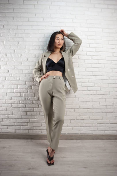 a fashionable asian woman in a stylish pantsuit poses against a white brick wall - fashion fashion model asian ethnicity tall imagens e fotografias de stock