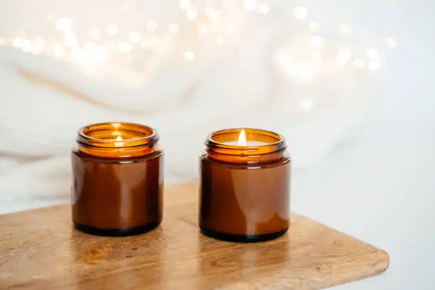 two burning candles in dark glasses on a wooden board. white background and garlands. good New Year spirit. holiday lights and candles.