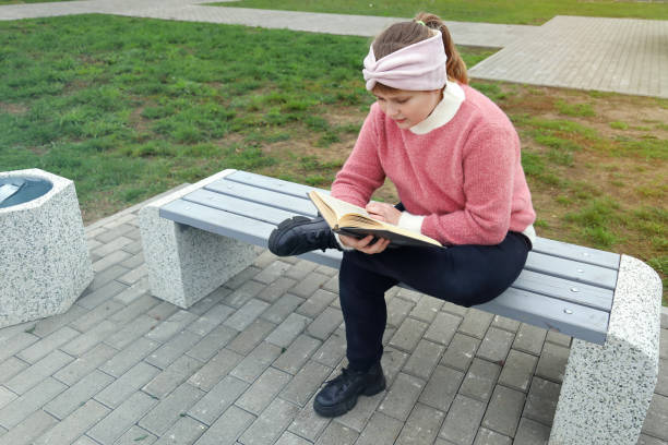 istock Chubby girl sits on bench and reads book in park 1355693370