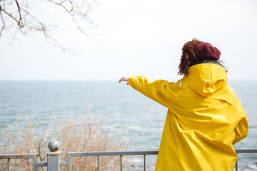 Woman in yellow raincoat showing at something at sea