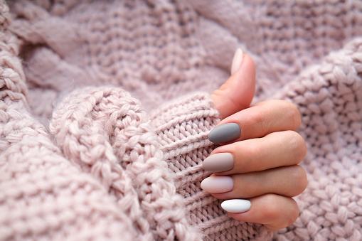 Manos de mujer con una hermosa manicura ovalada mate en un cálido suéter de punto. Tendencia invernal, esmalte de uñas beige con esmalte de gel, goma laca. Espacio de copia. photo