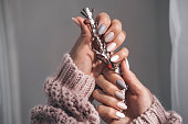 Women's hands with a beautiful matte oval manicure in a warm knitted sweater. Hands are holding a winter branch. Varnish beige nails with gel polish, shellac. Copy space.