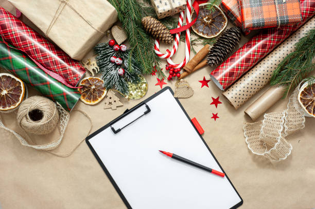 istock Shopping and christmas gift list. View from above. A table filled with materials for packing and decorating gifts and a white sheet with a marker for lists. 1355693922
