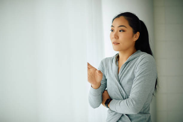 istock Pensive Asian woman looking through the window. 1355695991