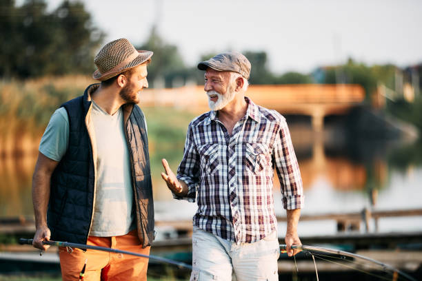 istock Senior fisherman communicating with his son while walking by the lake. 1355696141