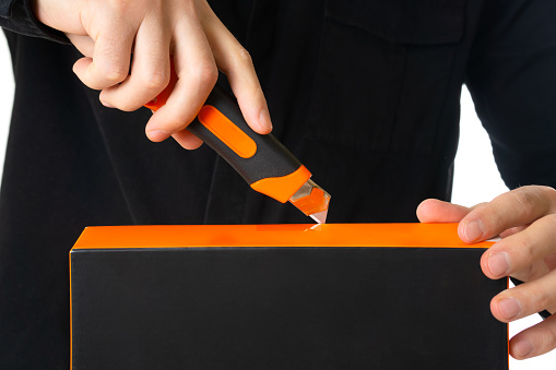 Man in black uniform using a retractable utility knife to open a sealed product box.