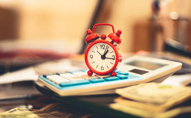 istock A red alarm clock on a blue calculator with US dollar bills in composition. 1355698104