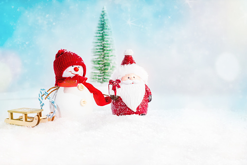 Figurines of Santa and a snowman in the snow on a light background with a Christmas tree and wooden sledges.christmas doll.